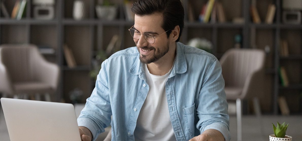 Smiling businessman in glasses using laptop, calculating bills, managing finances, happy young man planning budget, sitting at desk at home, browsing online banking service, satisfied by money refund